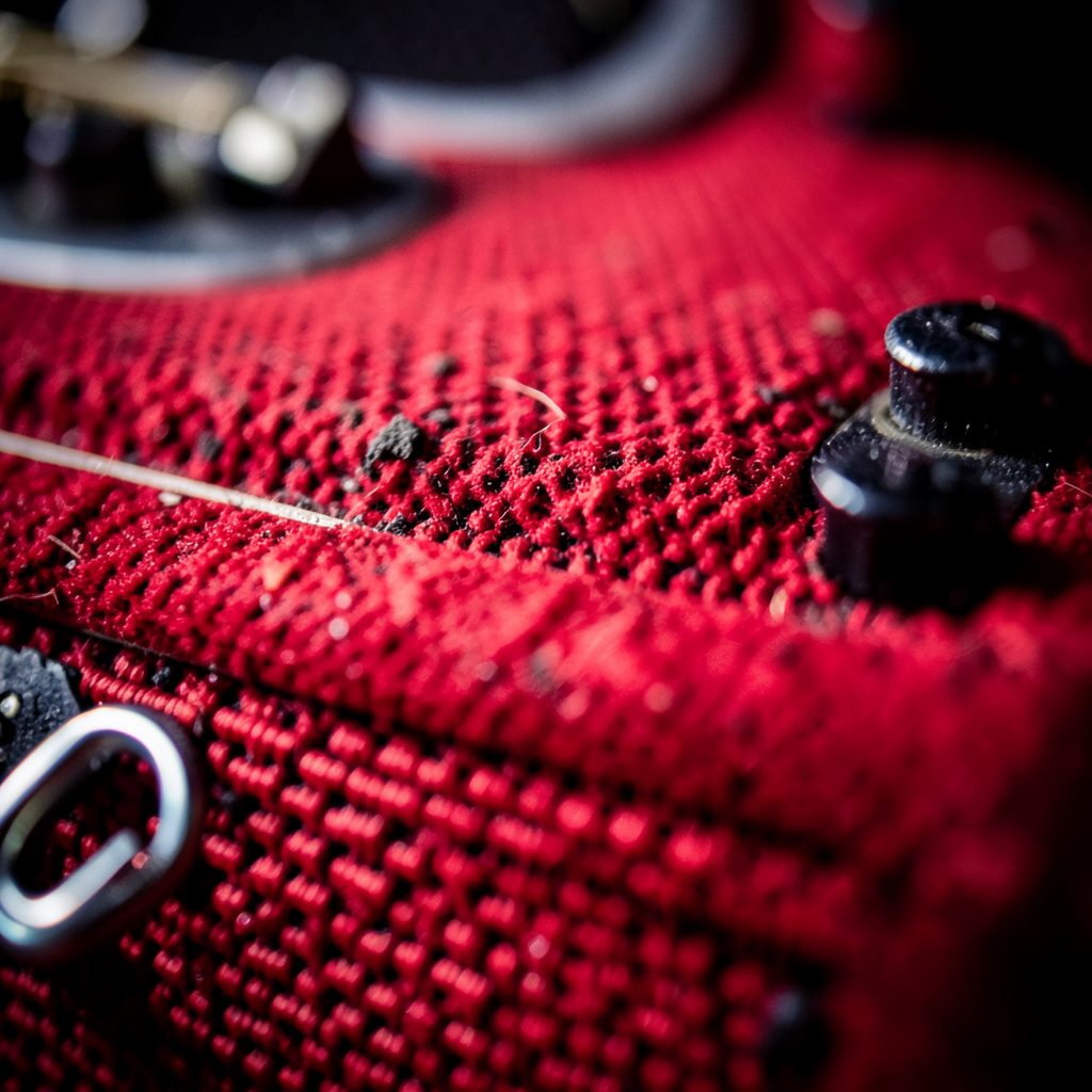 Atmospheric extreme close-up of a bass guitar pickup and black matte hardware, framed by deep amber wood grain in soft studio lighting.