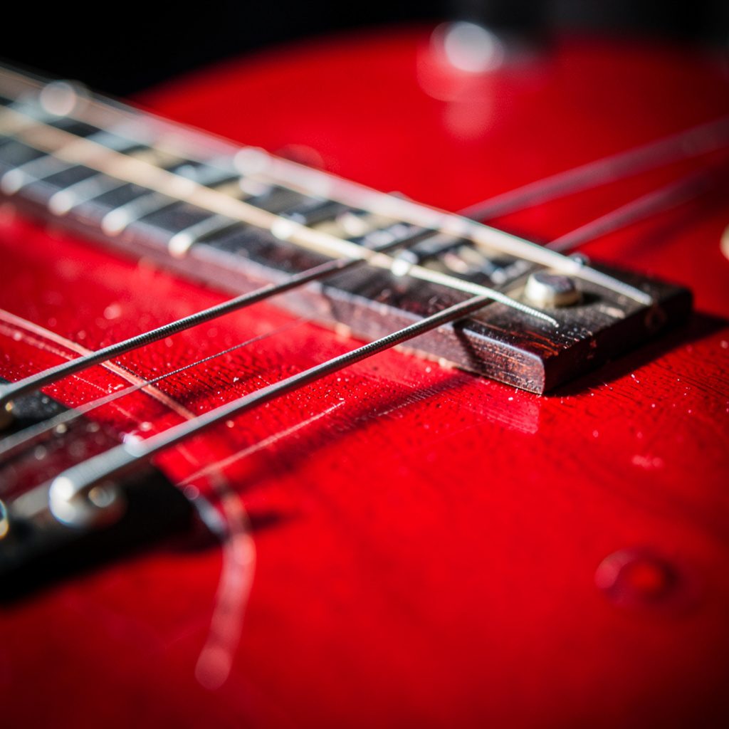 Close-up of a glossy electric guitar body with deep red and black burst finish, polished wood grain catching warm light