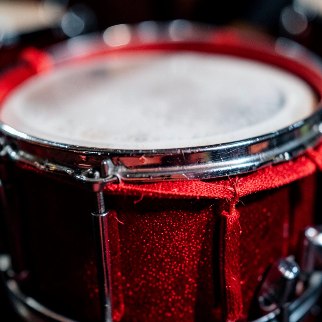 An extreme close-up photograph of a drum kit's maple wood grain, warm amber and caramel tones with a soft matte sheen, evoking a focused and intimate studio atmosphere.